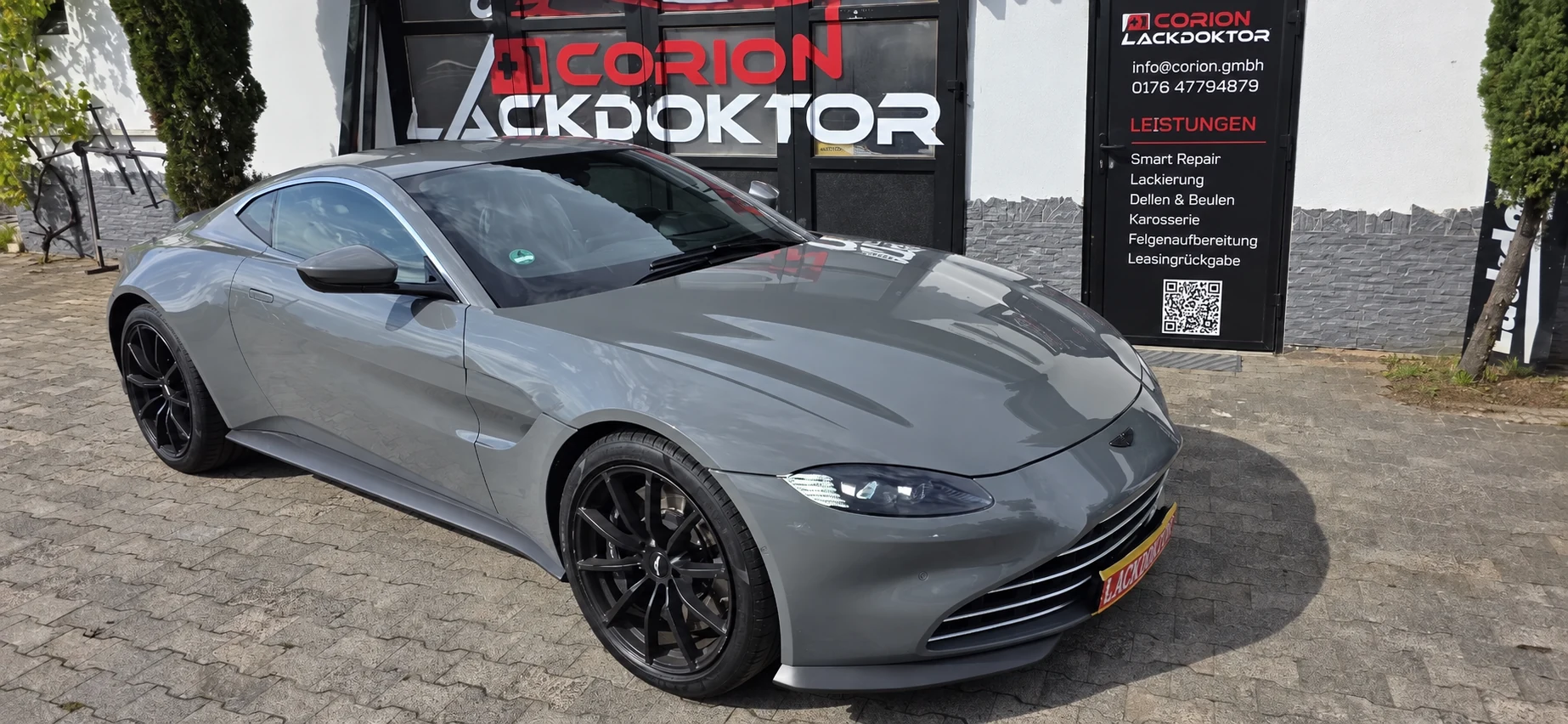 Grauer Aston Martin vor dem Corion Lackdoktor-Atelier; Türbeschriftung digital überarbeitet